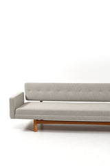 Soffa i grå / beige slitstarkt tyg med underede i ljust trä. Soffans rygg har klädda knappar.