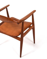 Karmstol av Hans J Wegner i massiv brunt teak. Sits klädd i brunt läder, med patina.