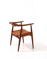Karmstol av Hans J Wegner i massiv brunt teak. Sits klädd i brunt läder, med patina.