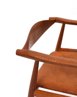 Karmstol av Hans J Wegner i massiv brunt teak. Sits klädd i brunt läder, med patina.