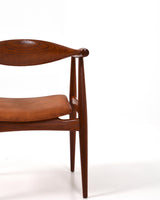 Karmstol av Hans J Wegner i massiv brunt teak. Sits klädd i brunt läder, med patina.