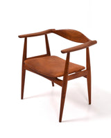Karmstol av Hans J Wegner i massiv brunt teak. Sits klädd i brunt läder, med patina.
