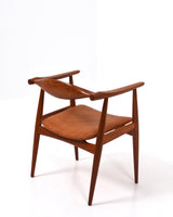 Karmstol av Hans J Wegner i massiv brunt teak. Sits klädd i brunt läder, med patina.