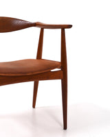Karmstol av Hans J Wegner i massiv brunt teak. Sits klädd i brunt läder, med patina.