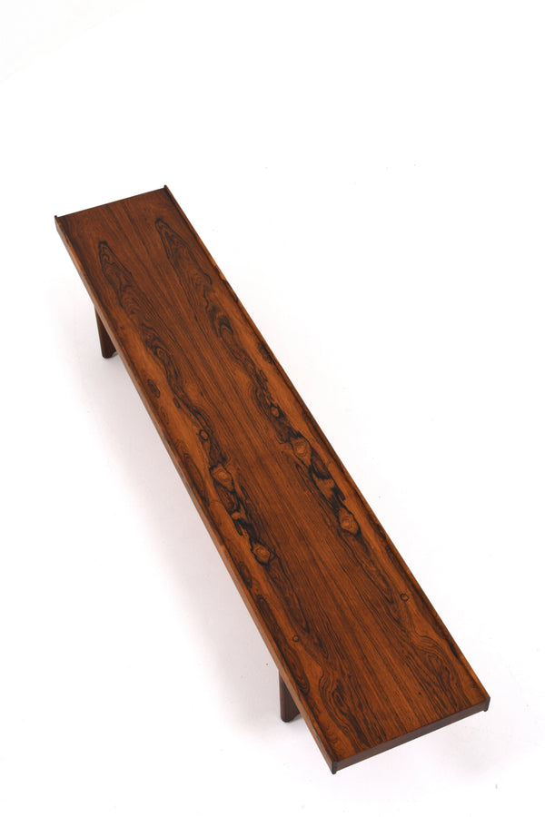 Lång och låg bänk i träslaget jakaranda. Färgen är brun med fina mönster i träet. 